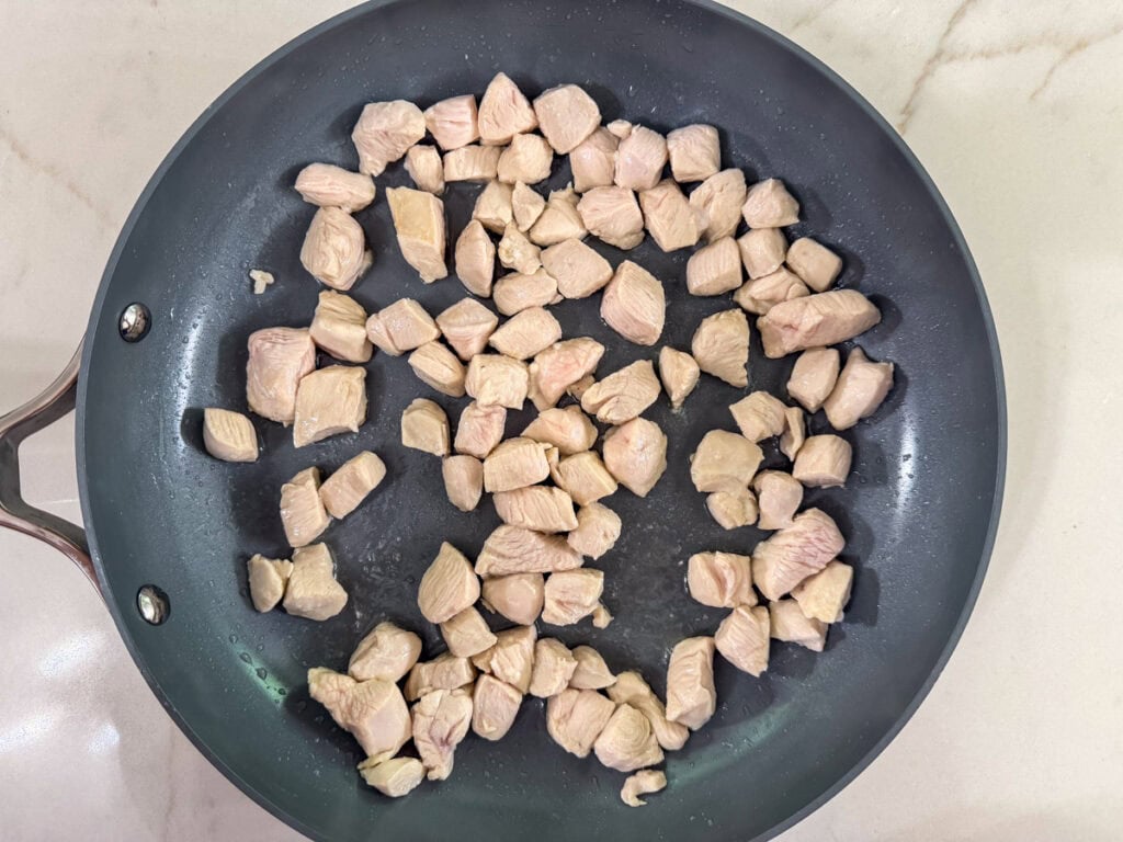 Diced chicken in a skillet after it's been lightly browned.