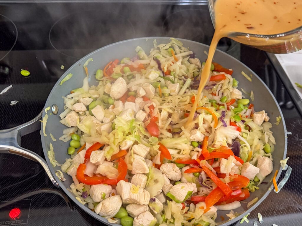 The sauce being added to the skillet with the chicken and vegetables.