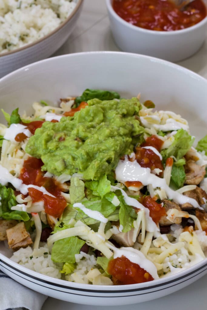 Closeup overhead of one Chipotle Chicken Burrito Bowl topped with guacamole and crema.