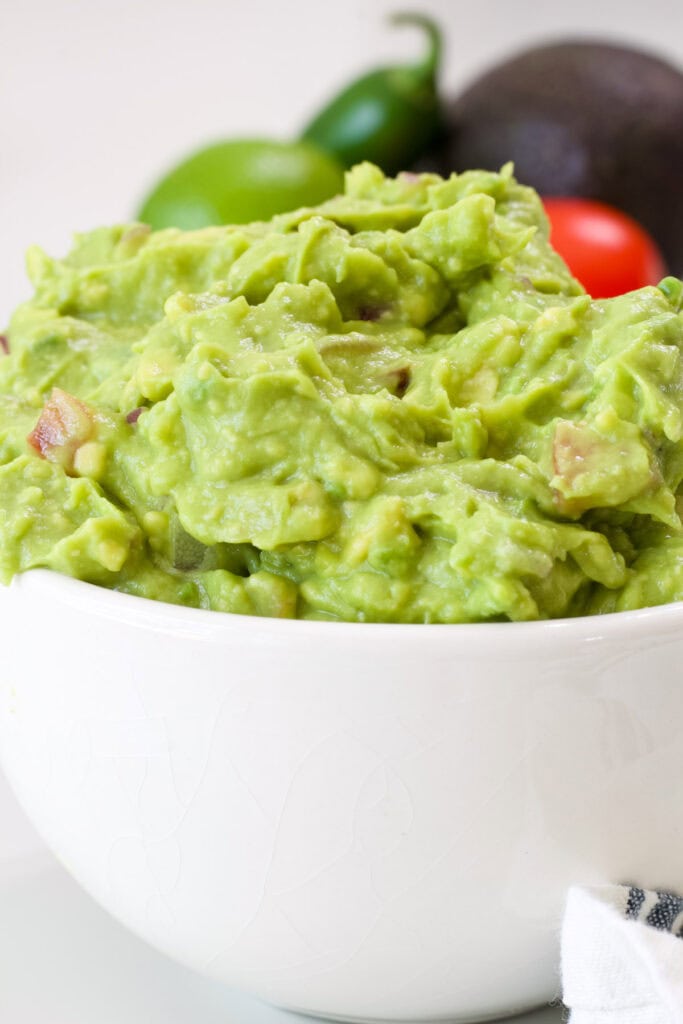 Side closeup view of a white bowl with homemade guacamole in it.