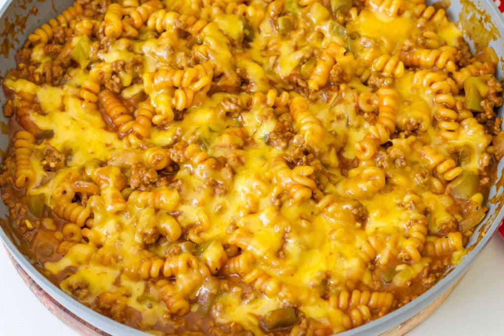 Overhead closeup of one pot sloppy joe pasta topped with melted cheddar cheese where a little over half the skillet is visible.