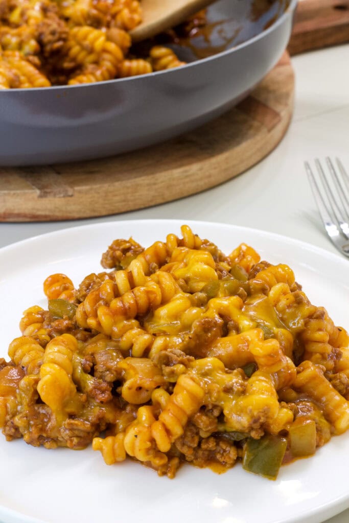 One serving of sloppy joe pasta on a plate and the pan with the remaining in the background.