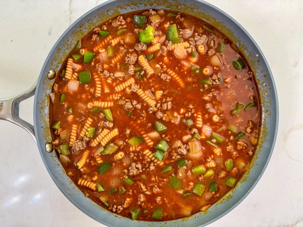 The beef broth, water and pasta added to the ground beef in the skillet.