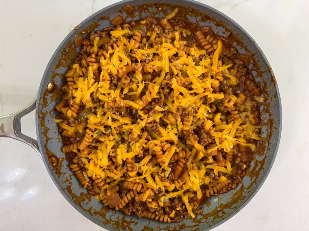 Shredded cheddar cheese on top of the sloppy joe pasta before it has melted.