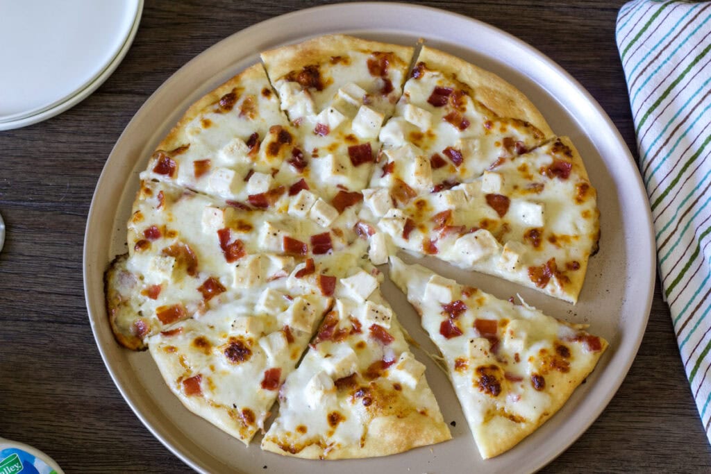 Closeup of an entire cut chicken bacon ranch pizza on a pizza pan with one piece moved out slightly from the pizza.