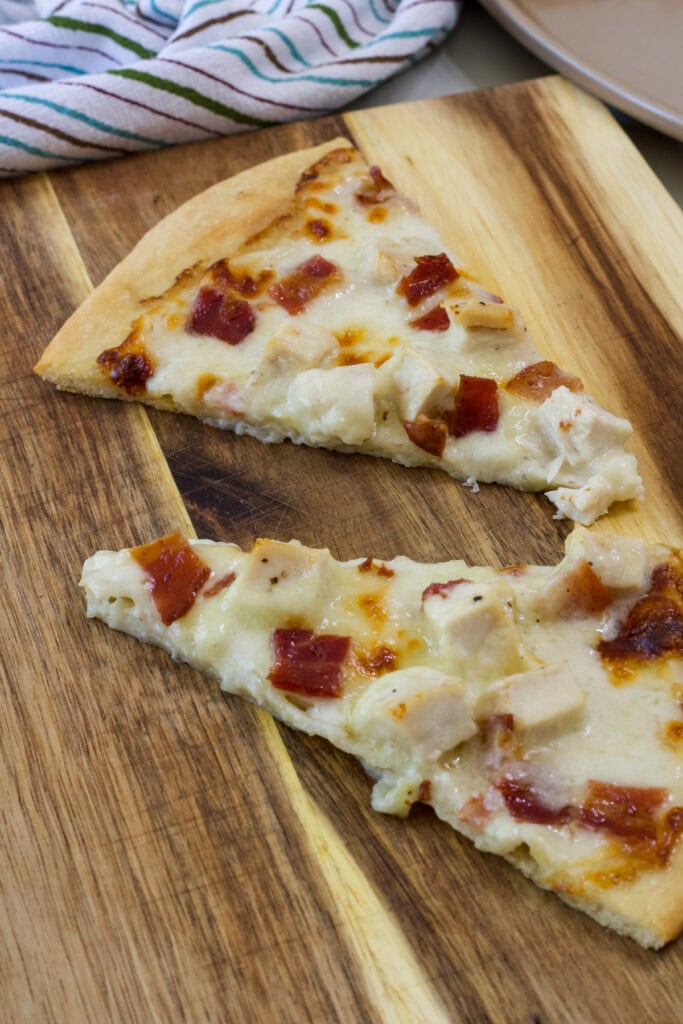 Two slices of chicken bacon ranch pizza on a wooden cutting board.