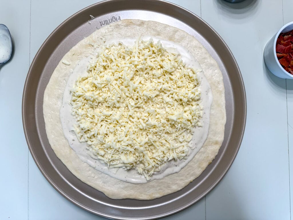 Pizza shaped pizza dough topped with creamy ranch dressing and freshly shredded mozzarella cheese.
