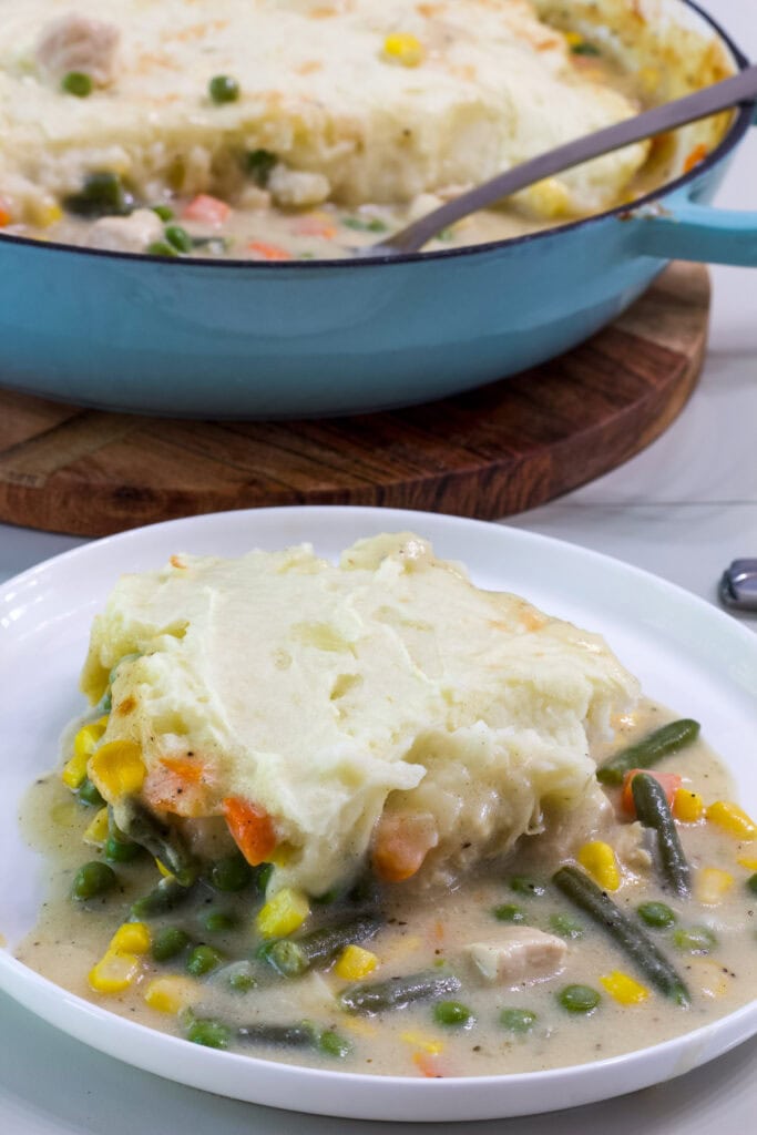 One serving of shepherd's pie with chicken in the foreground and the pan with the remaining shepherd's pie in the background.