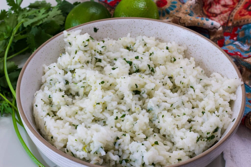 Closeup of a bowl of cilantro lime rice with fresh parsley and limes in the background.