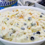 Very closeup overhead of cottage cheese fruit salad in a serving bowl and a container of cottage cheese in the background.