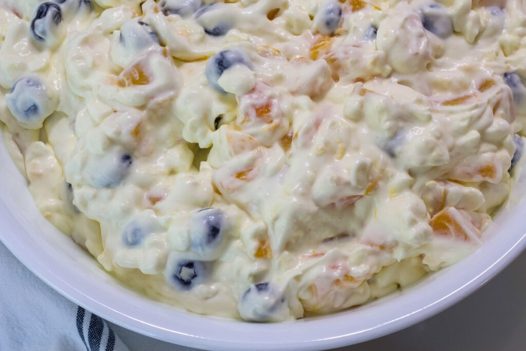 Closeup overhead shot of Cottage Cheese Fruit Salad with Peaches and Blueberries in a white serving bowl where only half is visible.
