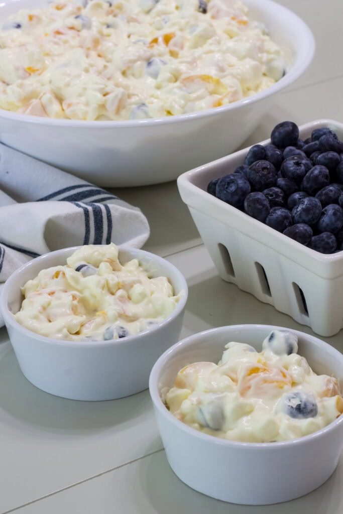Two small bowls of Cottage Cheese Fruit Salad with Peaches and Blueberries in front of a serving bowl with the remaining fruit salad and a basket of fresh blueberries.