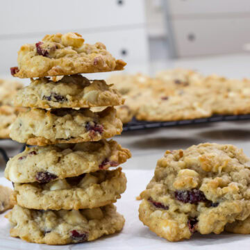 Closeup of a stack of six cowgirl cookies with a couple more cookies sitting next to the stack and a wire rack with many cookies on it in the background.