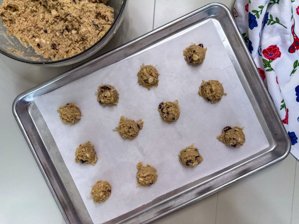 Twelve balls of cowgirl cookie dough portioned out on a parchment lined baking sheet ready to go into the oven.