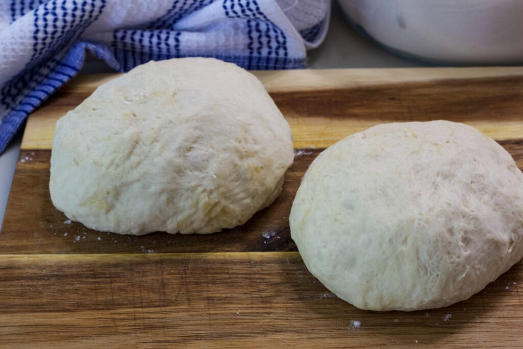 Two balls of no-knead pizza dough on a wooden cutting board.