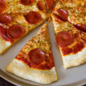 A pepperoni pizza with the one piece separated slightly from the whole pizza.