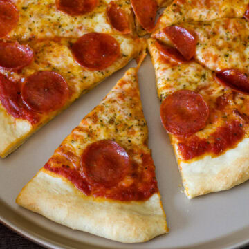 A pepperoni pizza with the one piece separated slightly from the whole pizza.