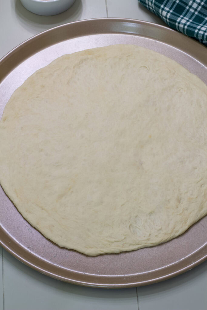Pizza dough spread out and ready for toppings on a pizza pan.