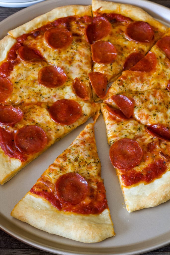A cut pepperoni pizza with one piece separated from the rest of the pizza.