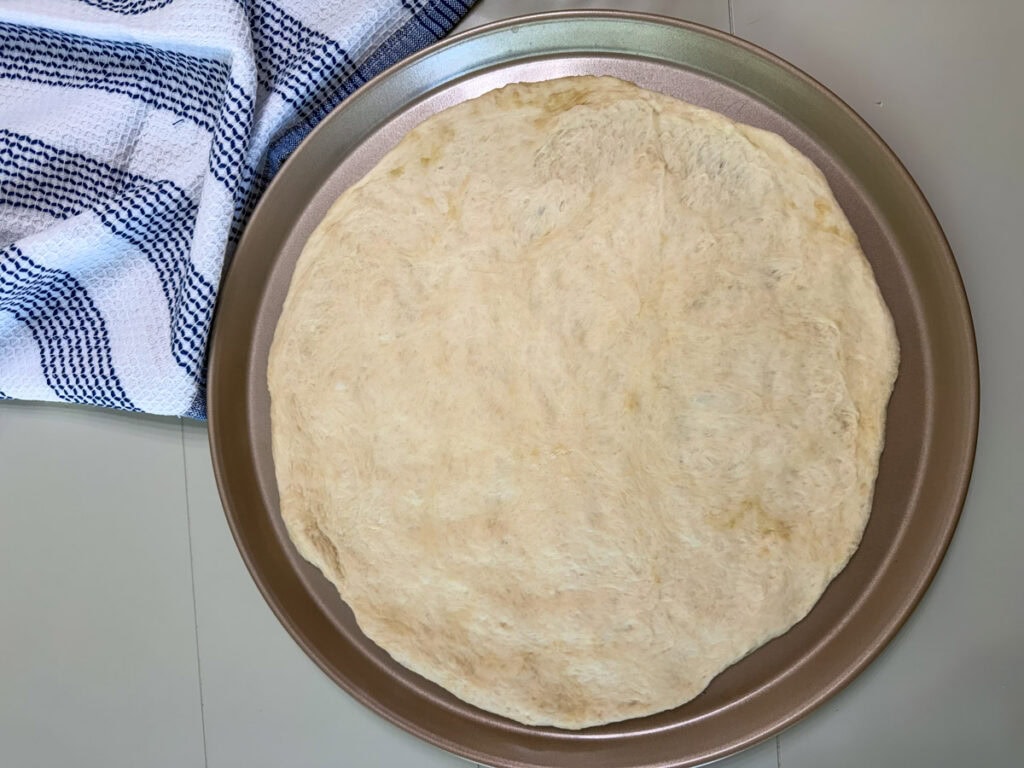 Pizza dough spread out on a pizza pan.