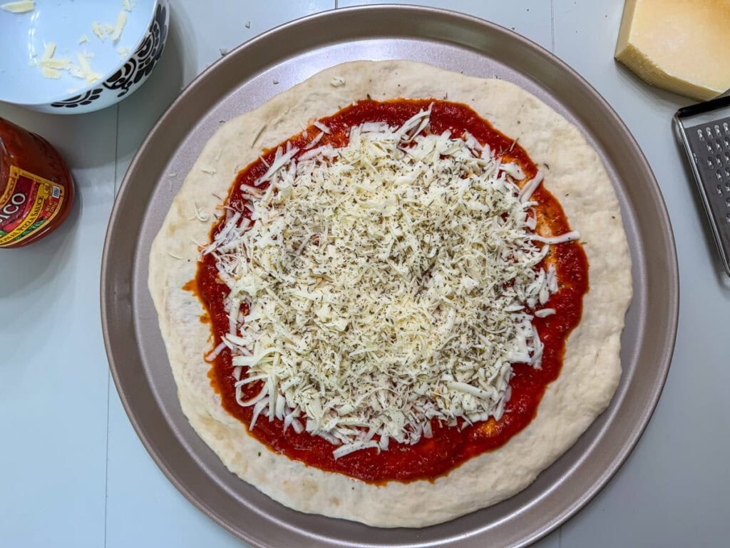 Shredded mozzarella cheese, Parmesan cheese, and Italian seasoning on top of the pizza sauce.