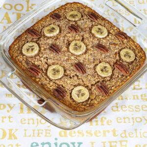 Closeup of a square baking dish with chocolate banana nut baked oatmeal topped with pecans and banana slices.