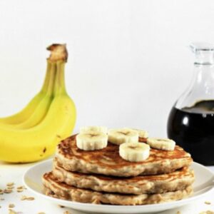 A stack of 3 oatmeal banana nut pancakes with sliced banana on top.