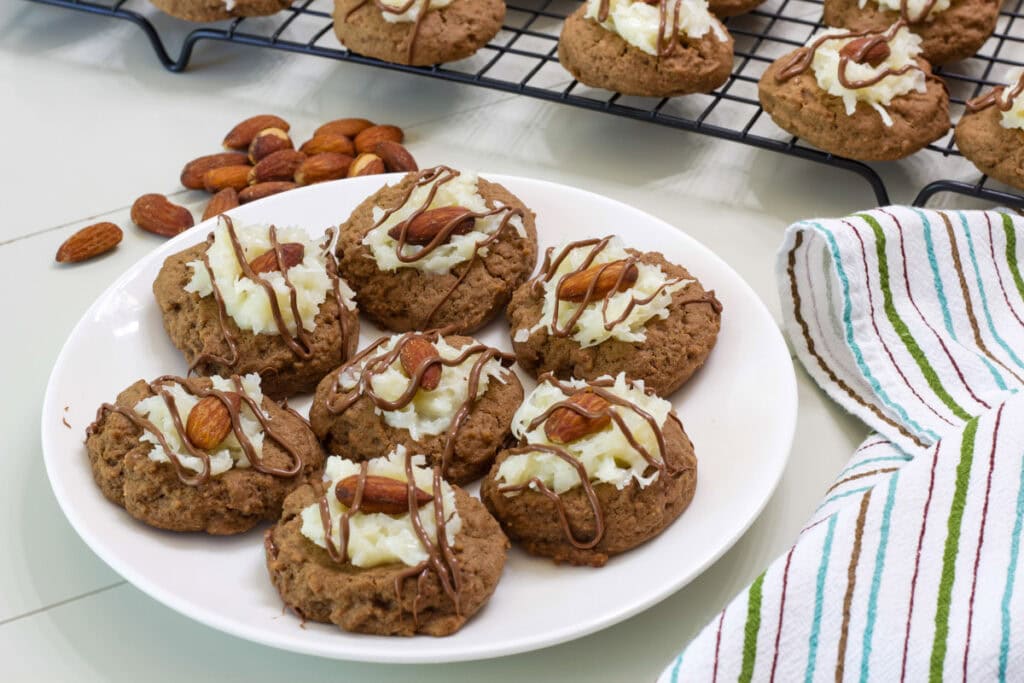 A plate of Almond Joy Cookies in the foreground and more cookies on a cooling rack in the background.