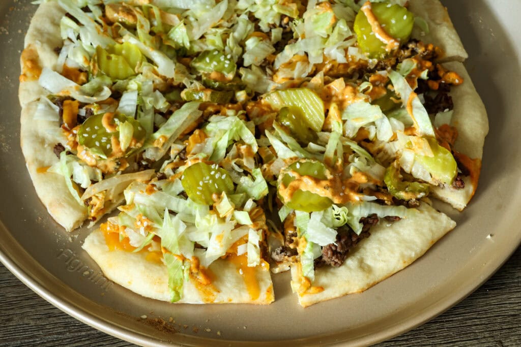 Closeup overhead of a half visible big mac pizza that has been sliced.