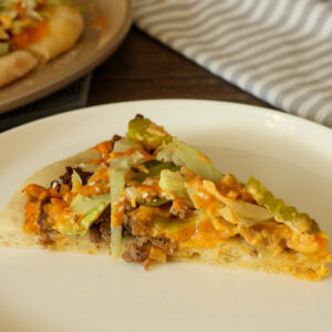 One slice of big mac pizza on a white plate.