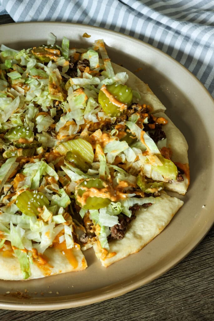 Side view of a partially visible sliced big mac pizza on a pizza pan.