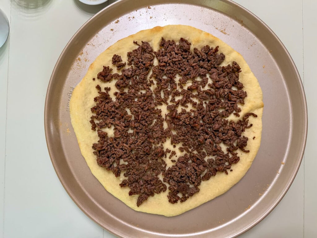 Par-baked pizza crust with browned ground beef on top.