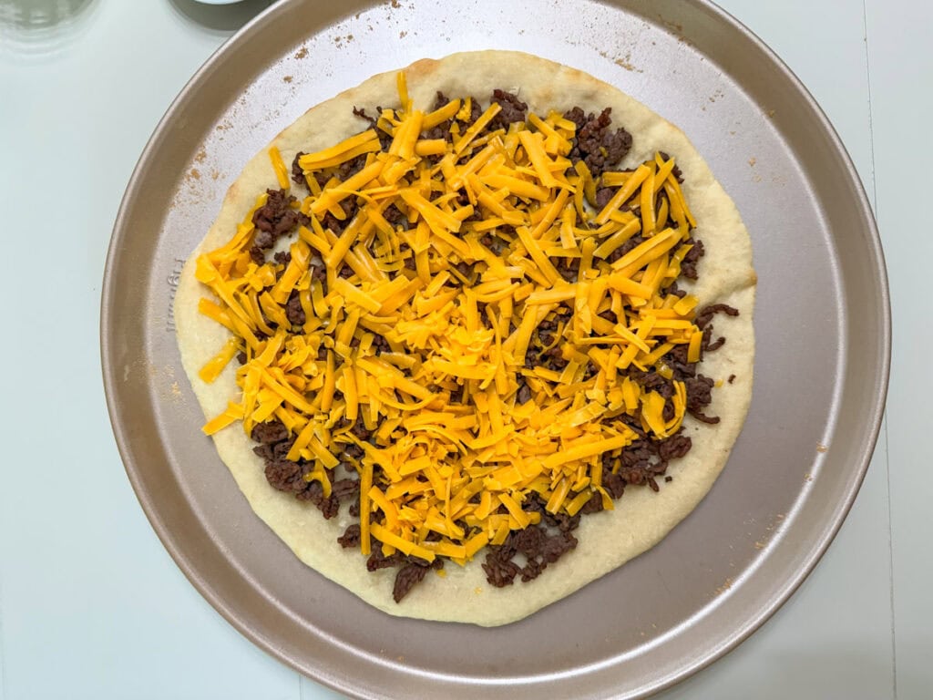 Shredded cheddar cheese on top of the browned ground beef.