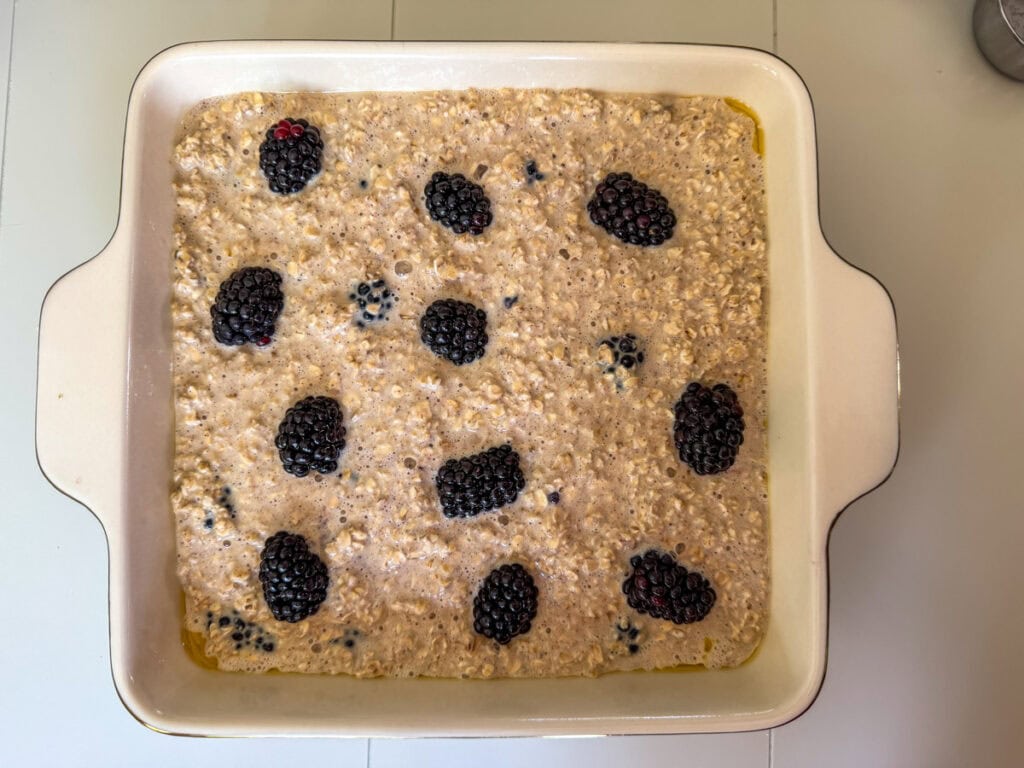The oatmeal mixture in a prepared square baking dish topped with blackberries and ready to go into the oven.