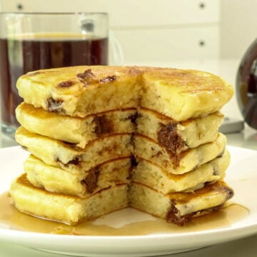 Side view of a stack of chocolate chip pancakes with a piece missing so the inside of all five pancakes is visible.