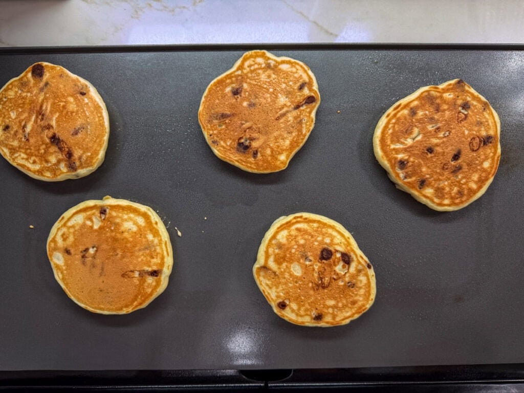 Five chocolate chip pancakes on a griddle after being flipped over.