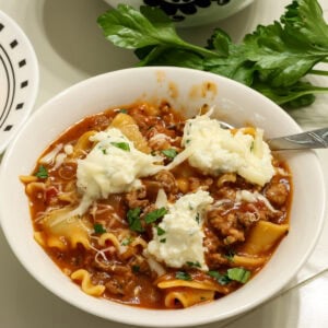 Closeup of one bowl of lasagna soup topped with dollops of ricotta cheese and chopped fresh parsley.