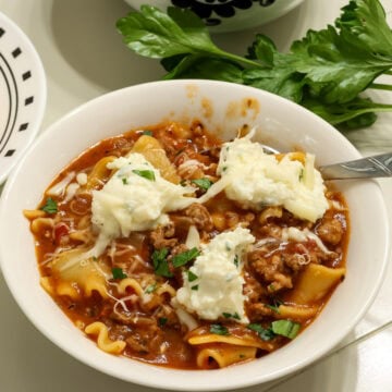 Closeup of one bowl of lasagna soup topped with dollops of ricotta cheese and chopped fresh parsley.