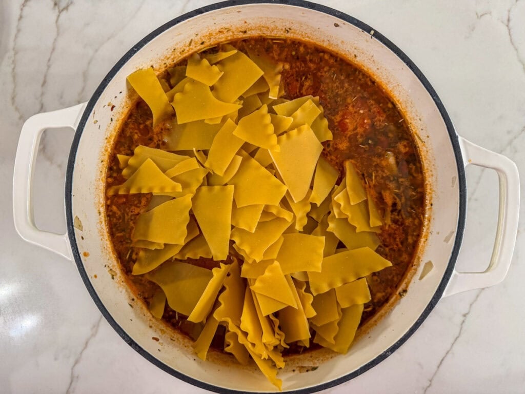 The broken lasagna noodles added to the meaty broth in a large pot.