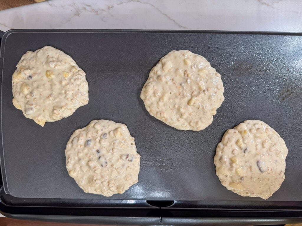 Four pancakes on a griddle before being turned over.