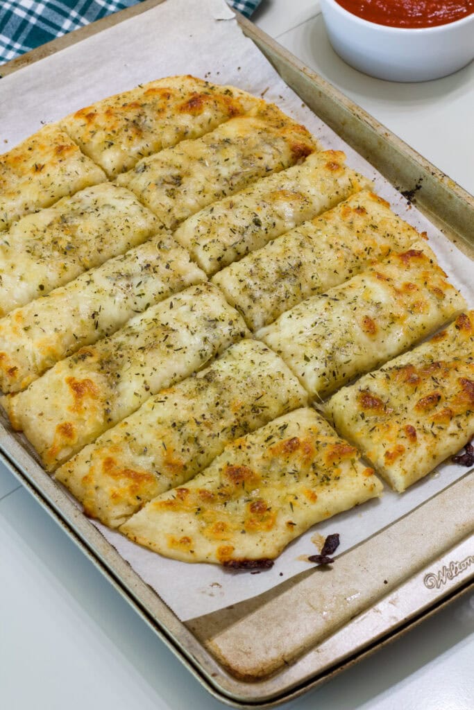 Closeup of a batch of cheese pizza dough breadsticks on a parchment lined baking sheet.