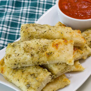 Very closeup up of breadsticks on a serving plate with marinara sauce.
