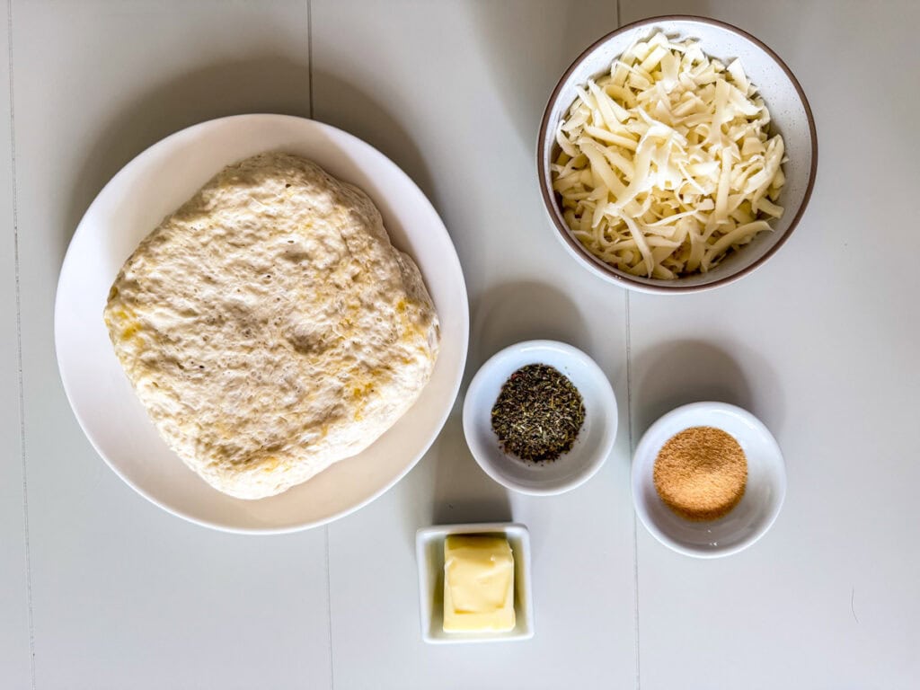 The pizza dough, shredded mozzarella cheese, butter, garlic powder and Italian seasoning measured out to make the pizza dough breadsticks.