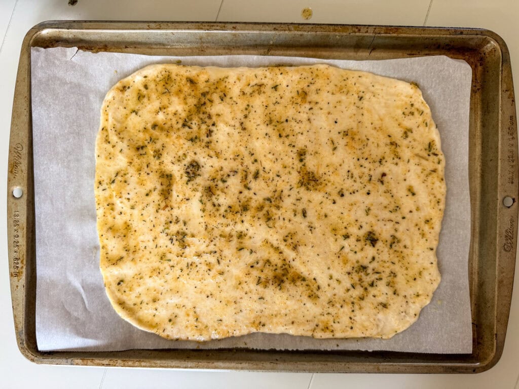 The spread out pizza dough with melted butter and spices on it.