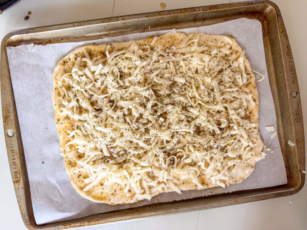Cheese and additional Italian seasoning on top of the buttered pizza dough so it's ready to go into the oven.