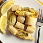 Closeup overhead of a serving of roasted hearts of palm and artichoke on a white plate.
