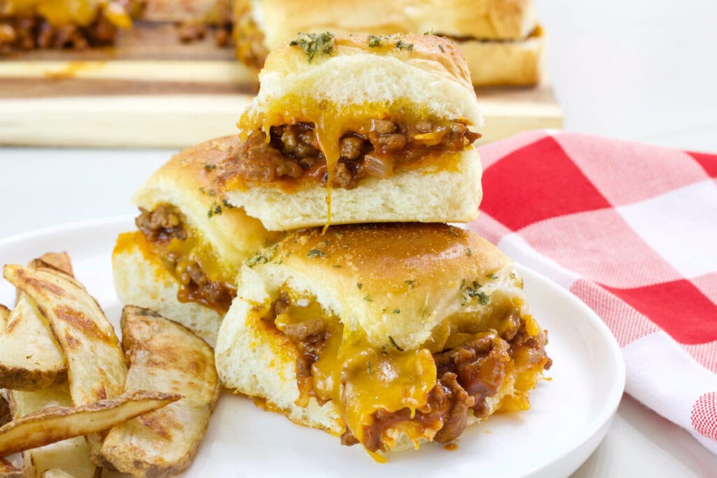 Three sloppy joe sliders on a white plate with some steak fries.