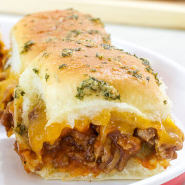 Very closeup side view of one cheesy Sloppy Joe Slider on a white plate.