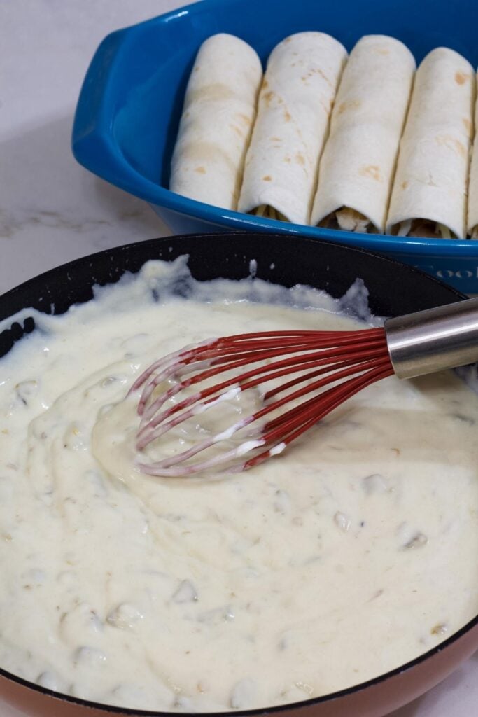 The sour cream enchilada sauce in a skillet and the rolled enchiladas in the background.
