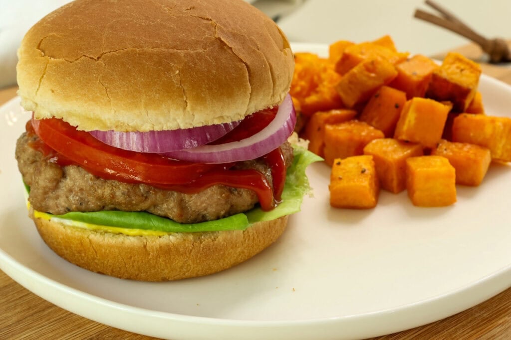 An air fryer turkey burger on a bun with toppings and sweet potatoes next to it.